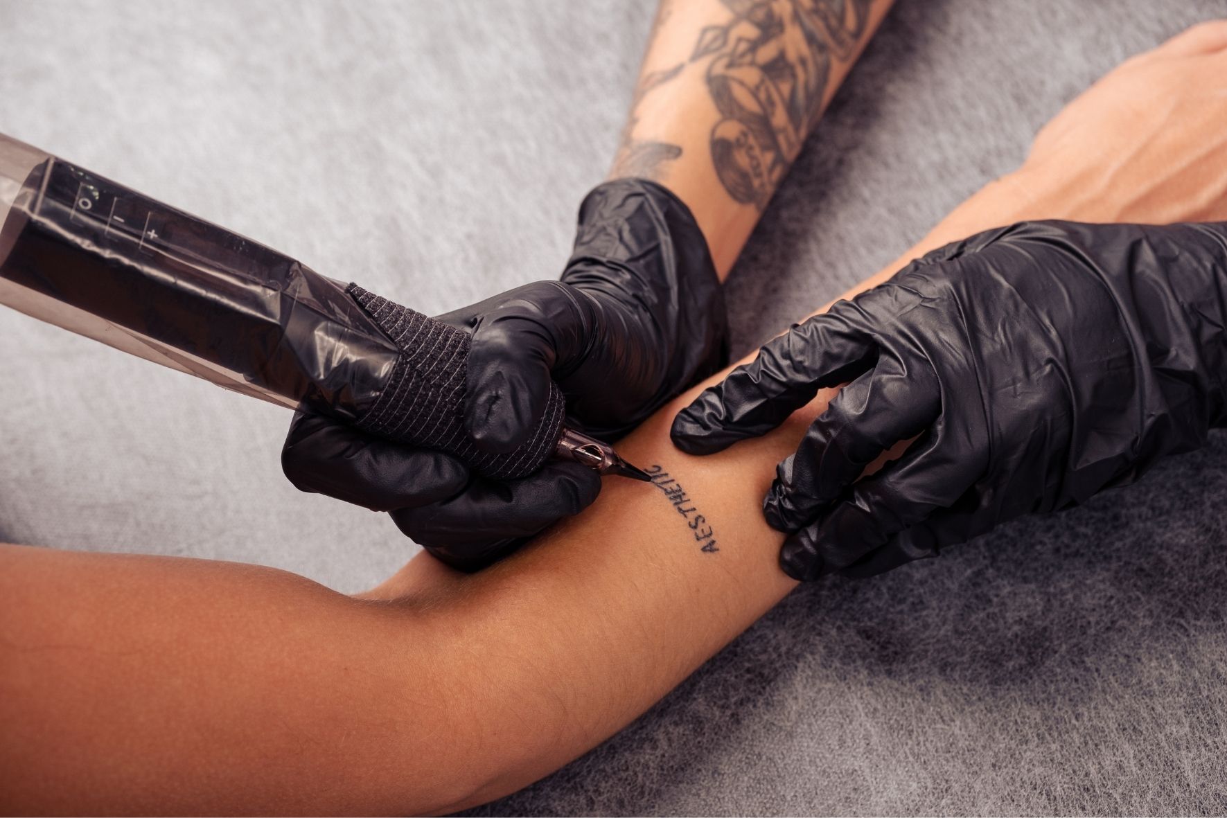 Main gantée utilisant une machine à tatouer sur l’avant-bras d’une personne dans un environnement de tatouage à Longueuil