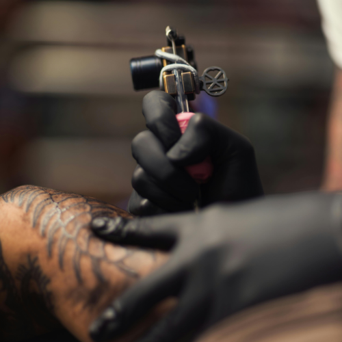 Machine à tatouer tenue par une main gantée au-dessus d’un tatouage coloré dans un salon de tatouage à Montréal-Nord